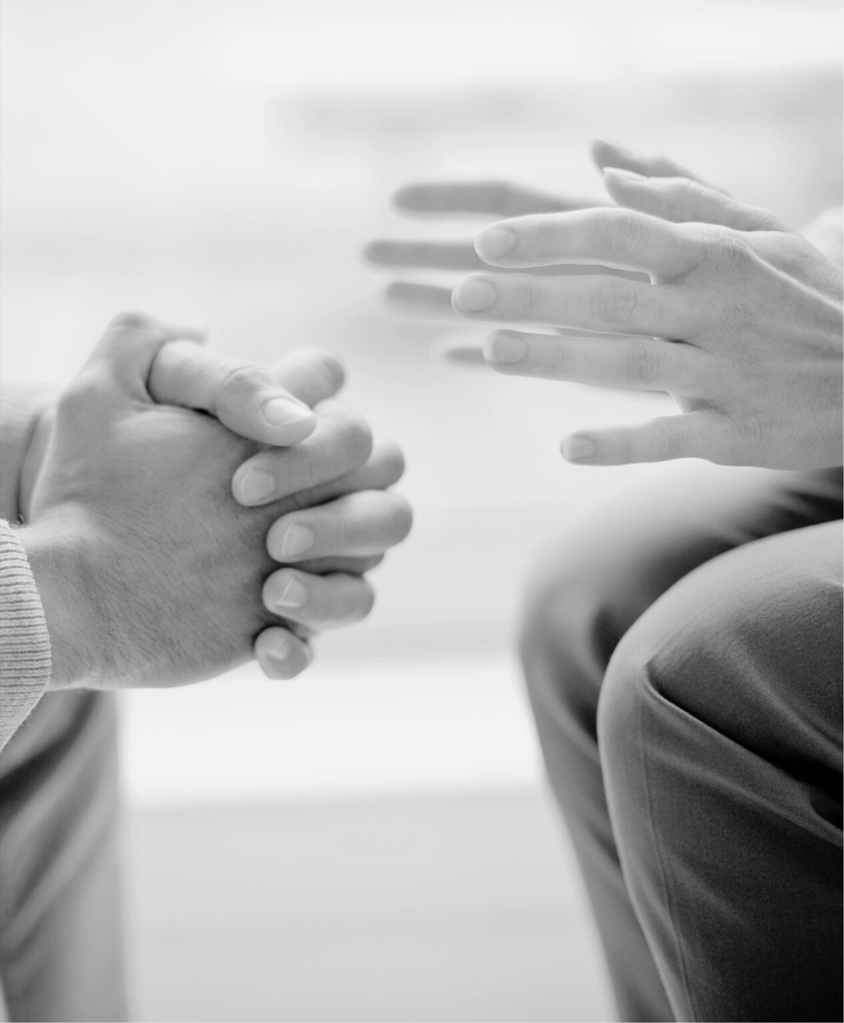 A counsellor's open hands facing a client's clasped hands mid-conversation.