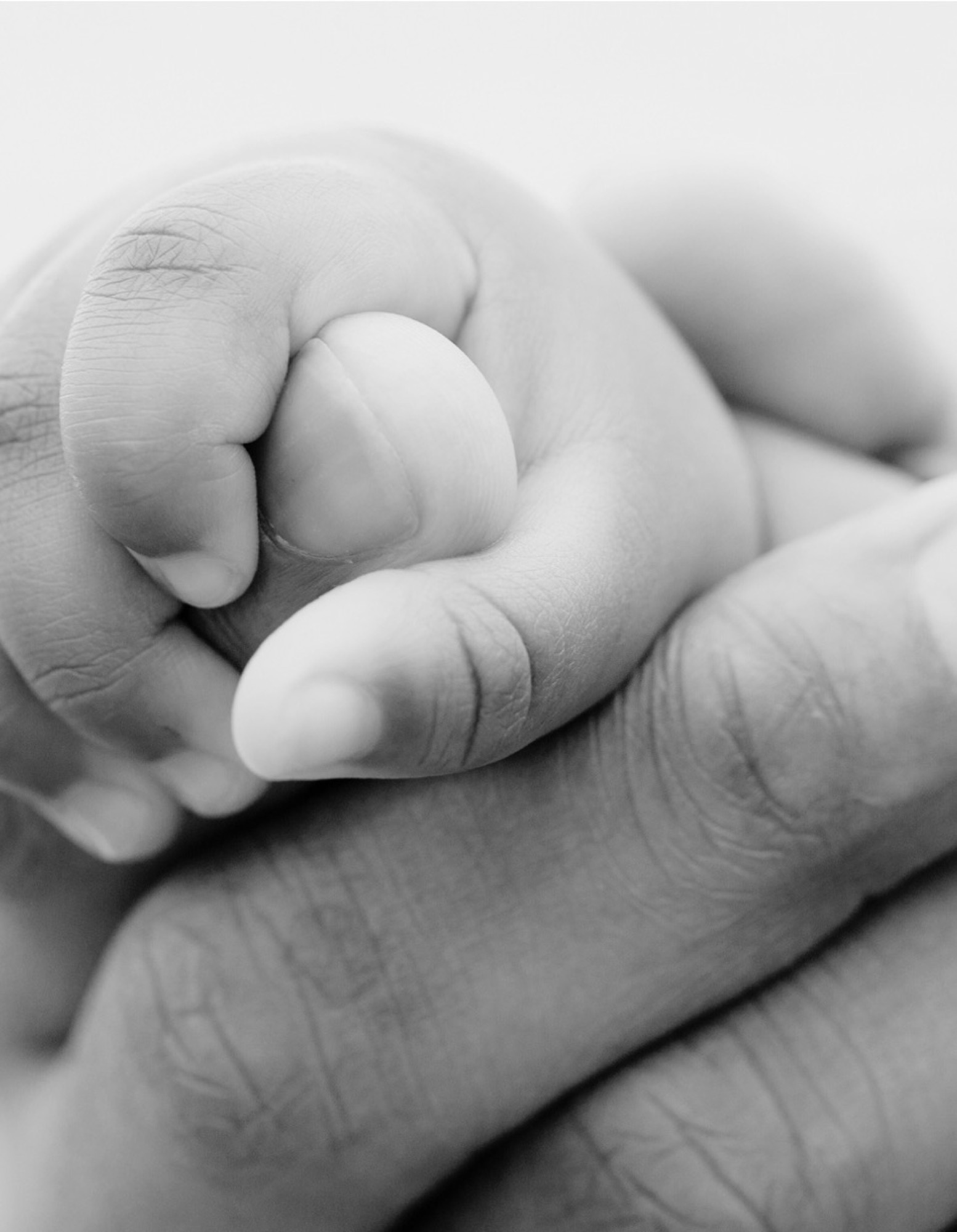 An adult hand cradling a tiny closed fist — the quiet weight of caring for someone.